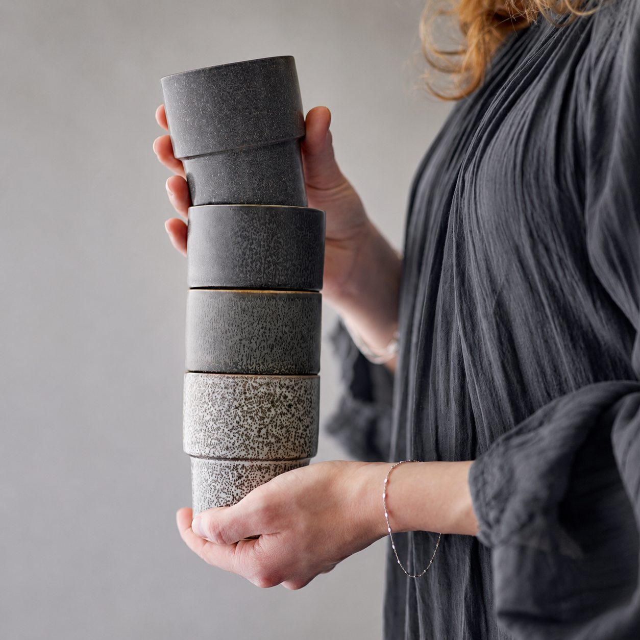 Handcrafted ceramic cups in earthy tones held in a natural lifestyle setting