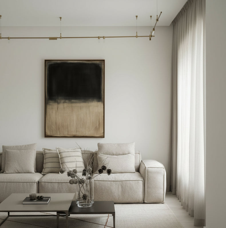 A modern living room scene featuring a large abstract wall art piece with a black-to-beige gradient, hung above a light beige fabric sofa with neutral throw pillows.