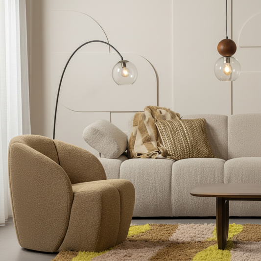 A modern living room scene featuring a beige upholstered modular sofa as the main product, styled with neutral throw pillows, a dark wood coffee table, a patterned rug, and pendant lights against a decorative cream wall.