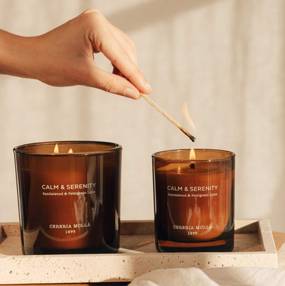 הדלקת נר בגפרור, מוקף בנרות Calm & Serenity על משטח עץ, מבית Cereria Mollà