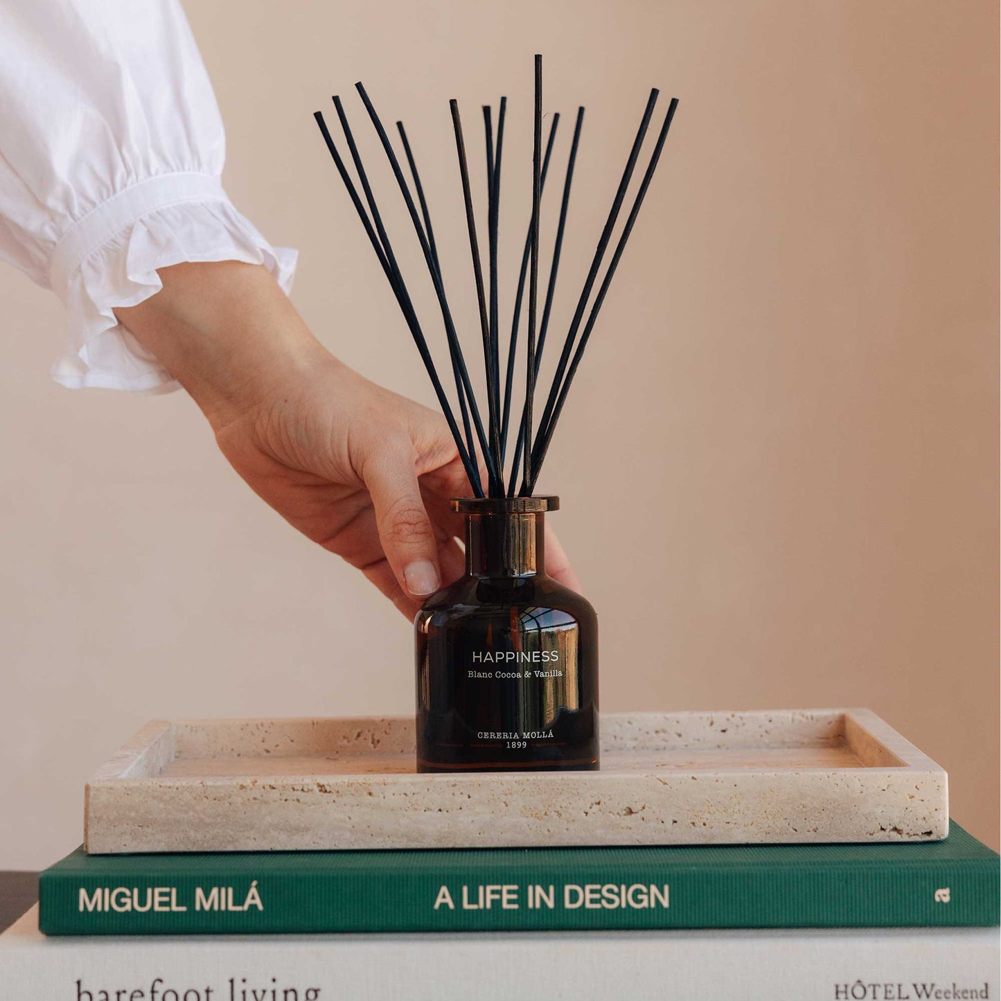 יד מחזיקה מפיץ ריח Happiness מעל ספרים, מבית Cereria Mollà